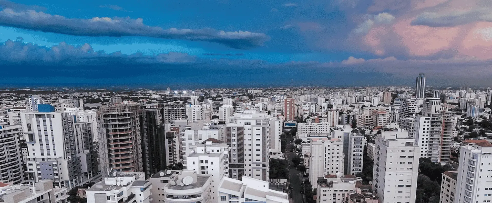 Skyscrapers stand tall in a dense urban area under a dramatic sky with a mix of blue and pink clouds, suggesting a transition between day and night.
