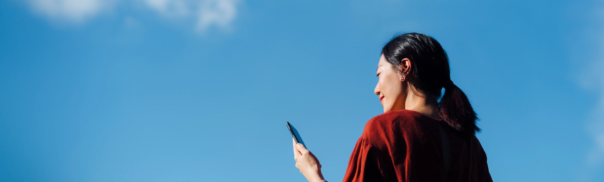 Woman using a smartphone outdoors under a clear blue sky.