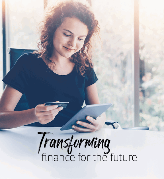 Young woman in a bright office with large glass windows, holding a tablet in one hand and a credit card in the other.
