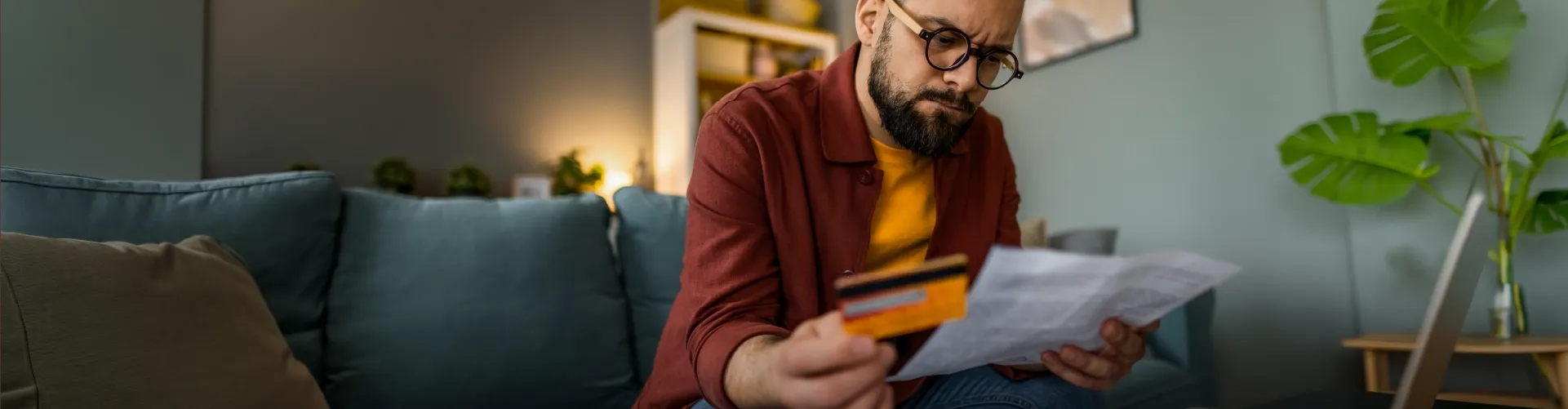 Man reviewing a bill while holding a credit card at home.