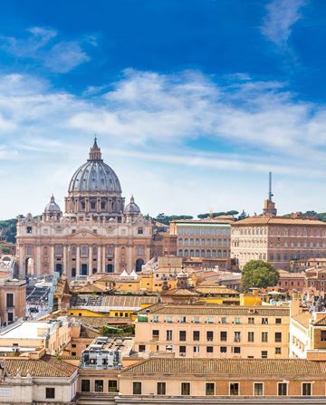 Vista della Basilica di San Pietro e degli edifici circostanti nella Città del Vaticano sotto un cielo azzurro.