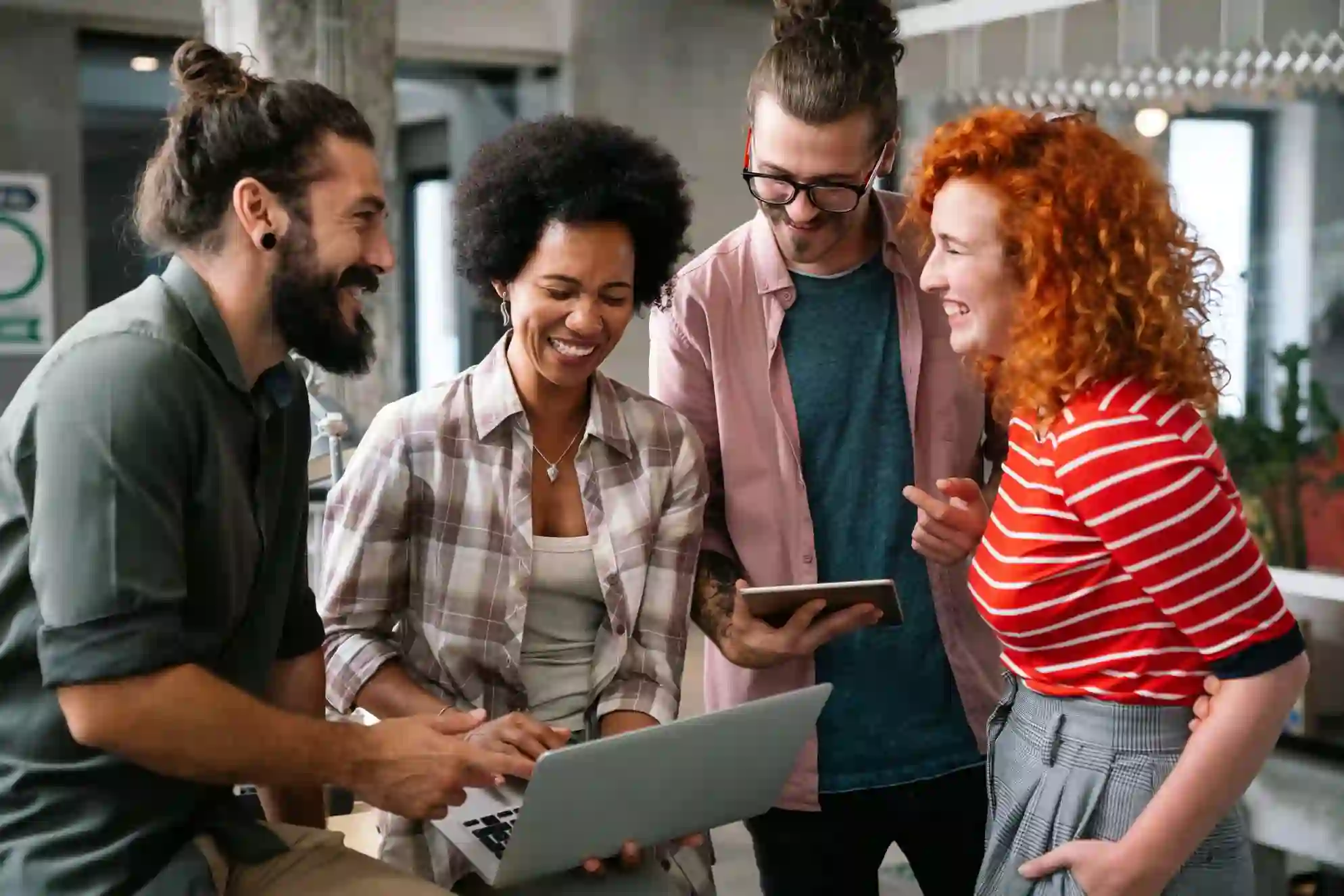 Four colleagues smiling and looking at a laptop together in an office setting.