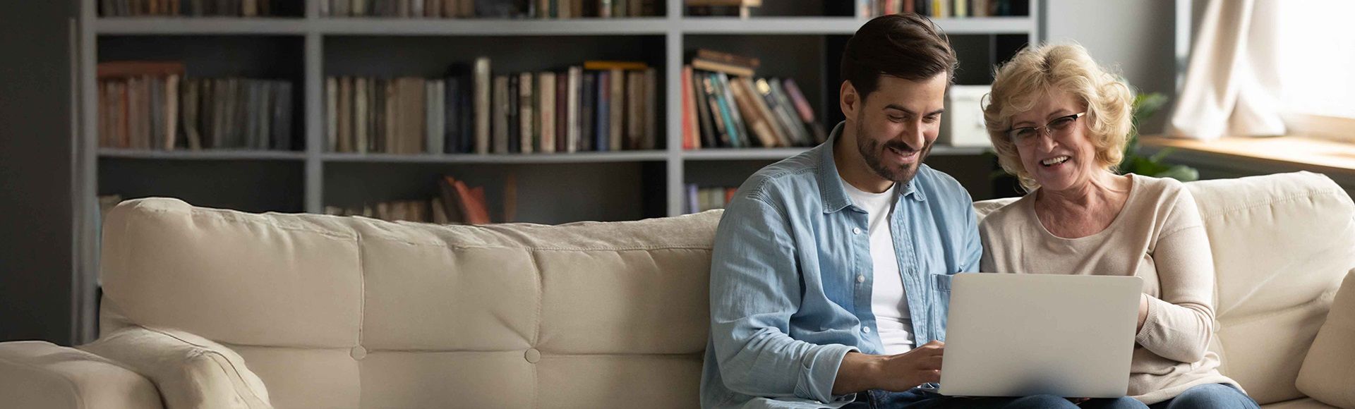 A young man and an elderly lady sit together on a sofa looking at a laptop. The image illustrates a blog about a healthcare leader saving 1.8M with an AI-powered omnichannel strategy.