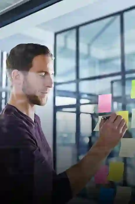 TP employee writing on a glass board with colorful sticky notes in an office setting.