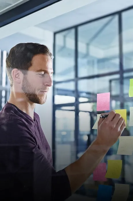 TP employee writing on a glass board with colorful sticky notes in an office setting. TP employee writing on a glass board with colorful sticky notes in an office setting.