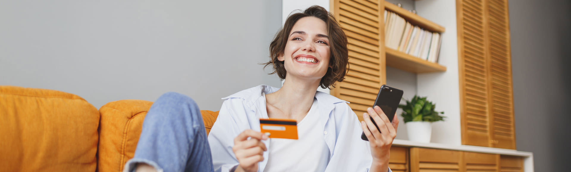 Smiling woman on a sofa holding a phone and credit card, showing trust in debt recovery.
