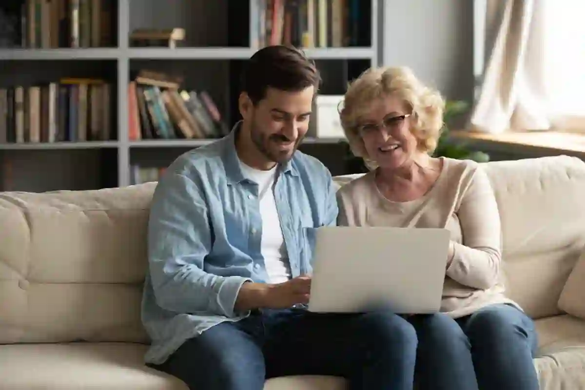 A young man and an elderly lady sit together on a sofa looking at a laptop. The image illustrates a blog about a healthcare leader saving 1.8M with an AI-powered omnichannel strategy.