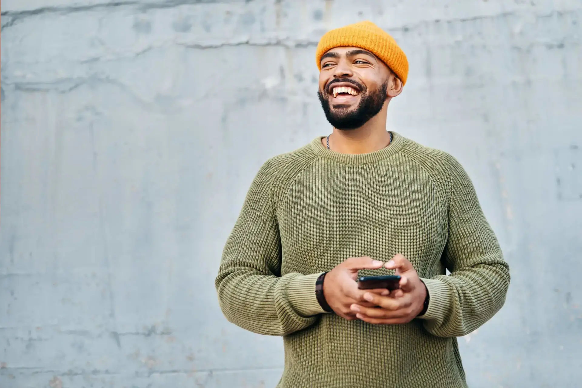 Smiling man in a beanie holding a phone, representing TP’s focus on connection and positive experiences.