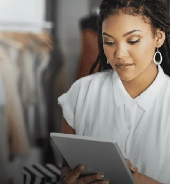 African saleswoman working on a tablet in a clothing store, illustrating TP’s Retail and E-commerce solutions.
