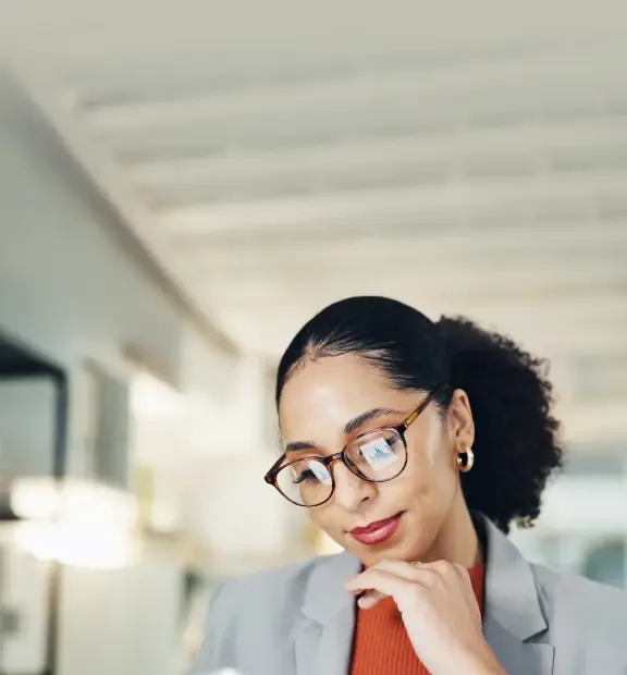 A professional woman thoughtfully analyzes data, with charts reflected in her glasses in a bright office.