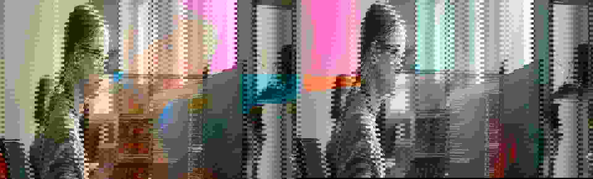Blonde woman wearing glasses focused on coding across dual monitors, illustrating the delivery of AI data services.