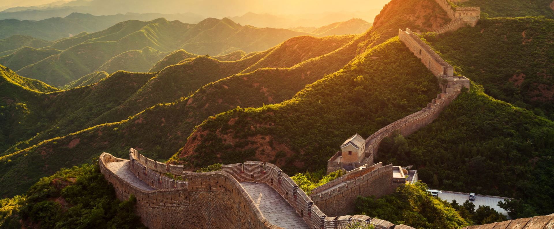 长城蜿蜒穿过绿色山脉，在日落时分，石墙在温暖的光线下闪耀。