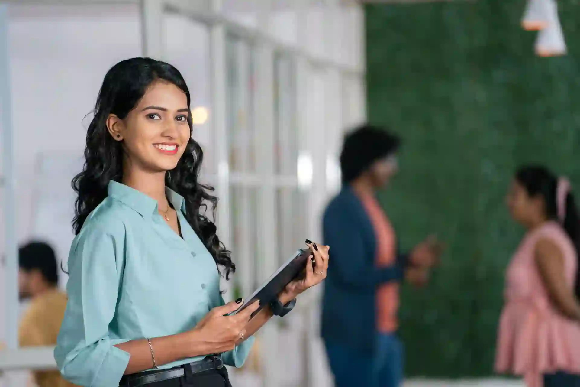 A young business woman holding a tablet inside a modern and green office