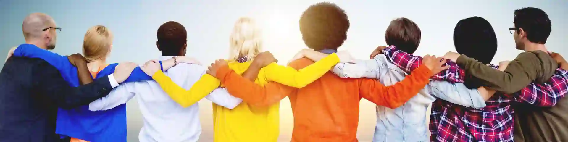 Diverse group of people standing together with arms around each other, facing the horizon.