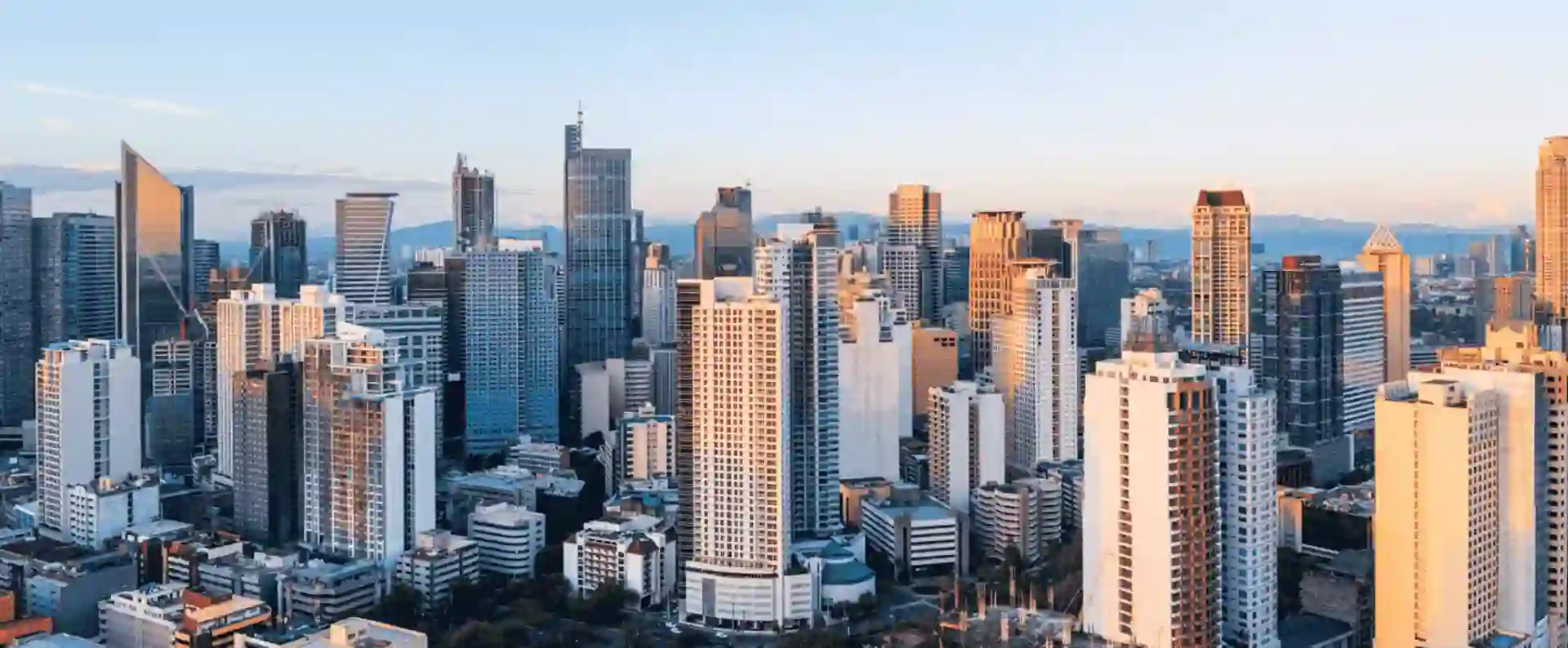 Modern skyscrapers under a clear sky with sunlight casting warm highlights across the cityscape.
