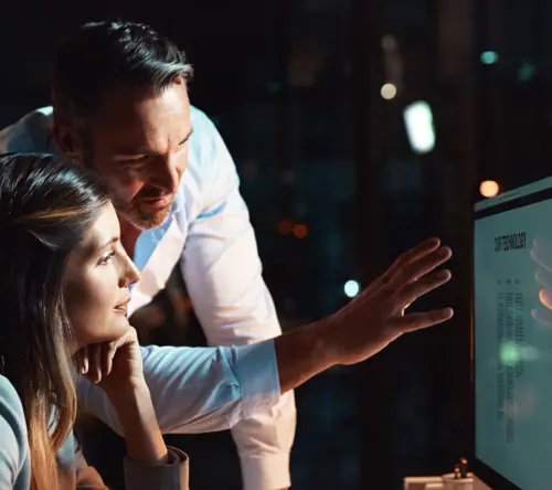 Colleagues analyzing data on a computer screen during a late-night work session.