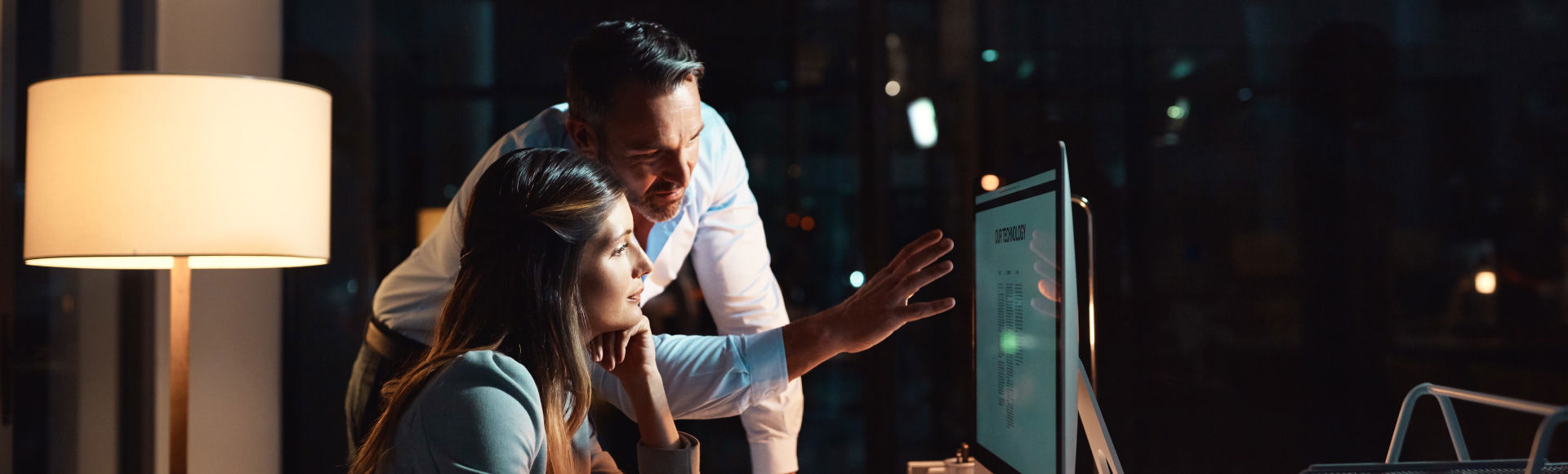 Colleagues analyzing data on a computer screen during a late-night work session.