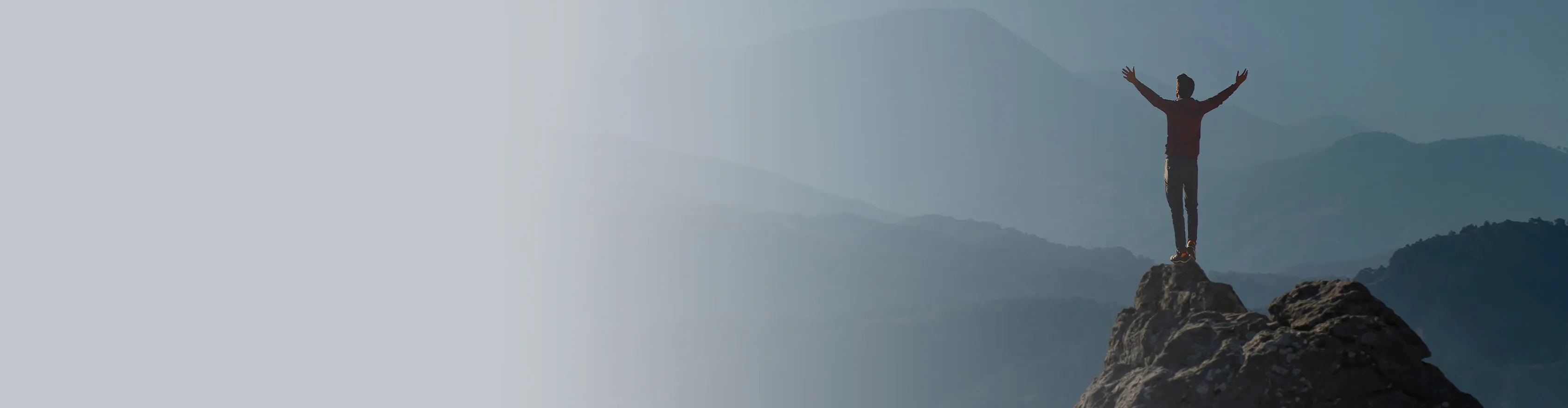 A lone hiker stands atop a rocky peak with arms outstretched, embracing the vast, mist-shrouded mountain ranges stretching into the distance. 