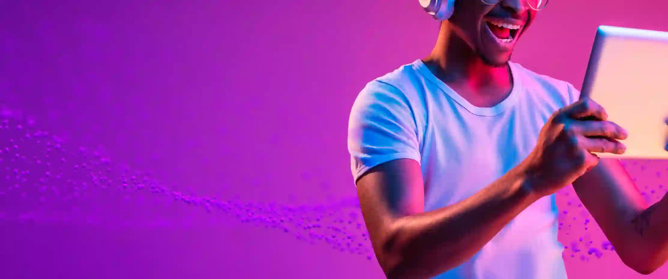Excited young man wearing headphones and using a tablet with vibrant purple background