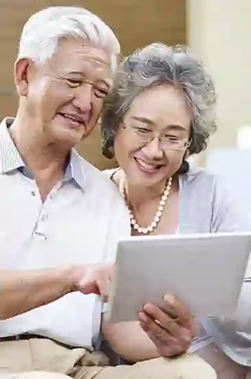 Cute Asian couple sitting together and reading on a tablet, sharing a quiet and cozy moment.