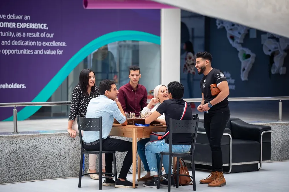 Group of young professionals smiling and talking around a table in a modern Teleperformance office. Group of young professionals smiling and talking around a table in a modern Teleperformance office.