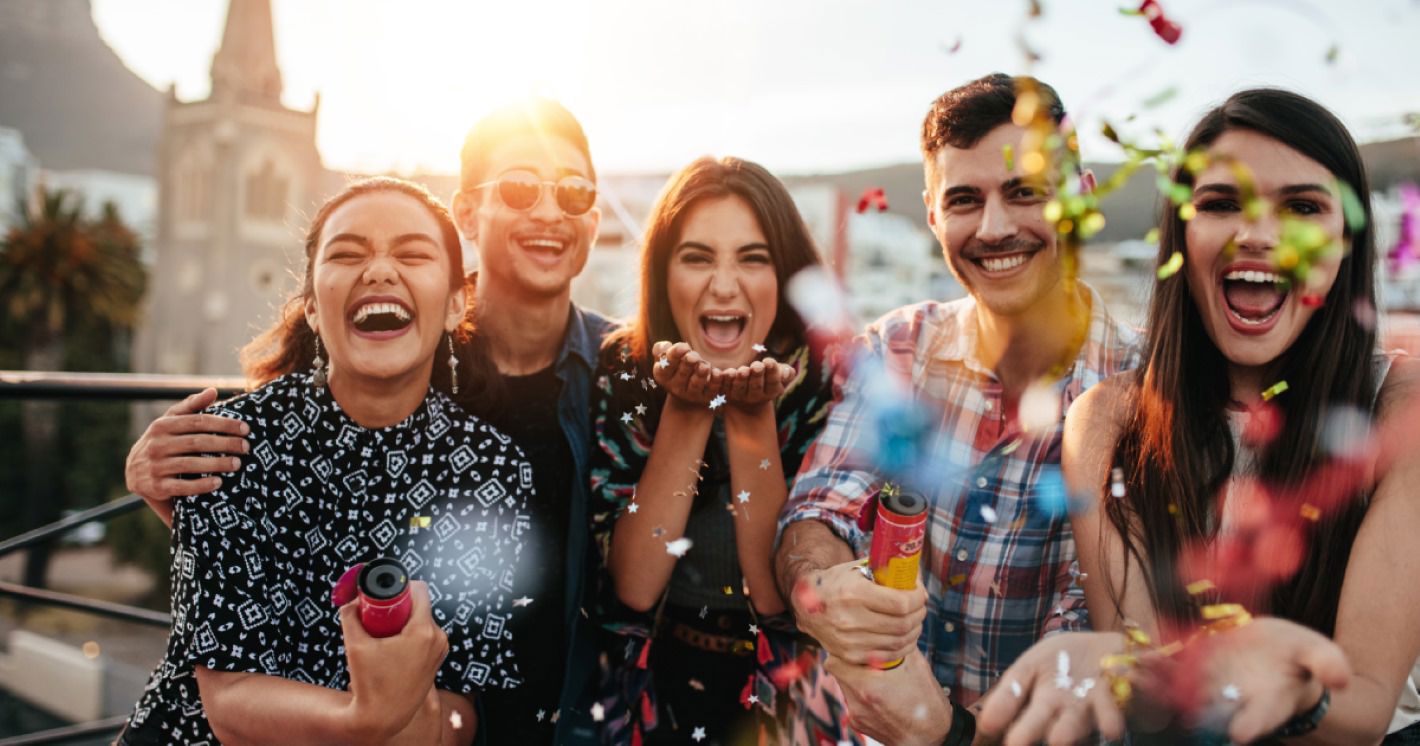 Group of young people celebrating outdoors with confetti and smiles.