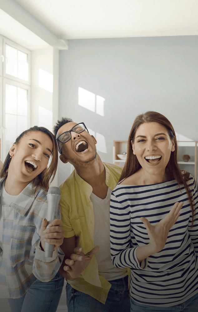 Three people sing joyfully together; one holds a microphone.