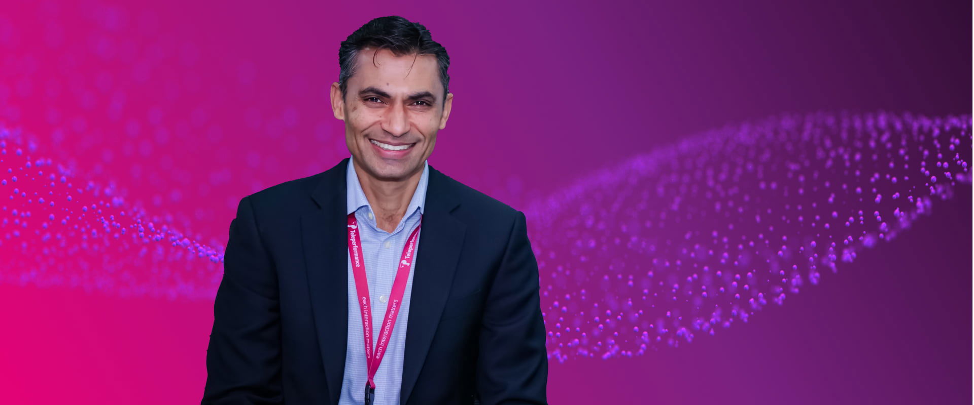 Smiling professional wearing a suit and Teleperformance lanyard, standing in front of a purple background with digital wave patterns. Smiling professional wearing a suit and Teleperformance lanyard, standing in front of a purple background with digital wave patterns.