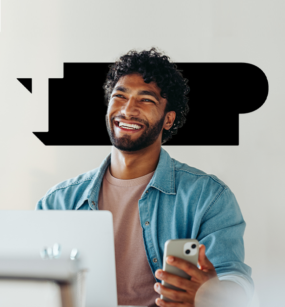 A person smiles while holding a smartphone. they are seated at a desk with a laptop. the word "top" is prominently displayed in bold black letters behind them.