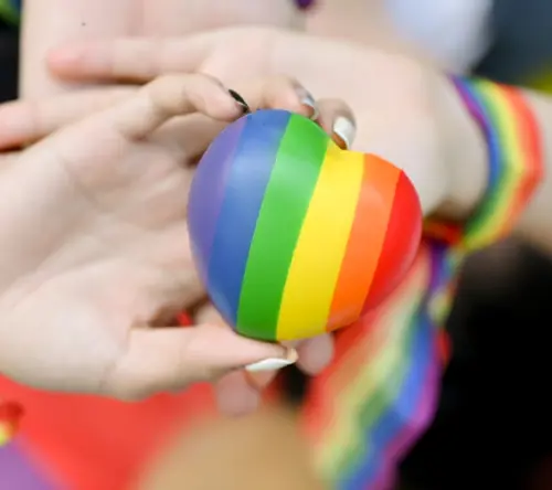 Hands holding an LGBTQ+ pride heart, representing belonging, inclusion, and respect.