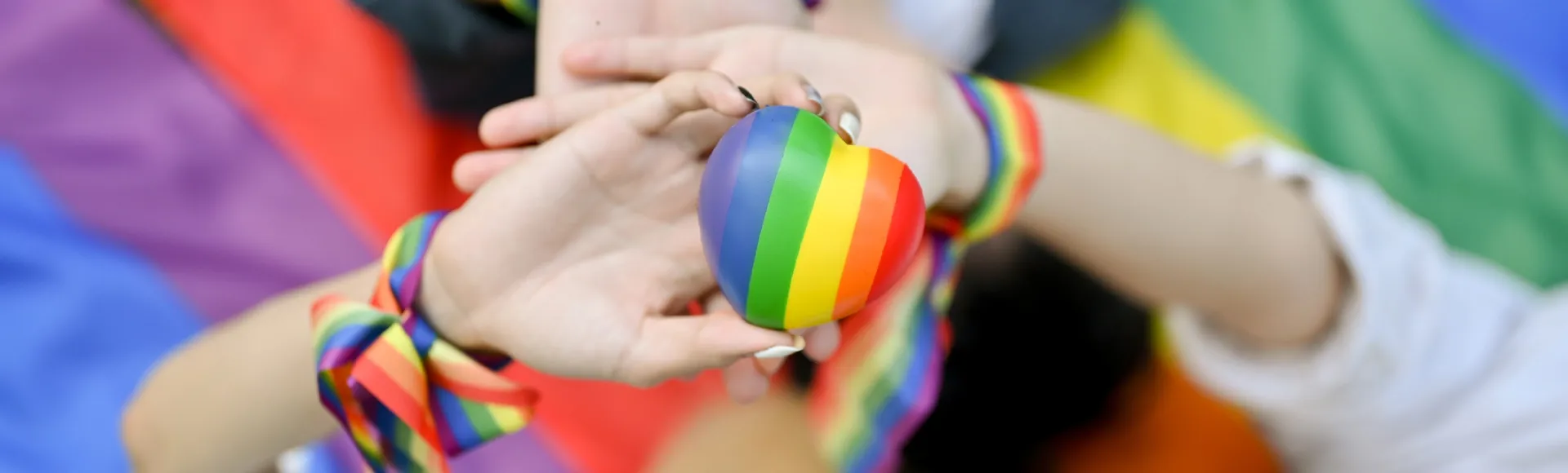 Hands holding an LGBTQ+ pride heart, representing belonging, inclusion, and respect.