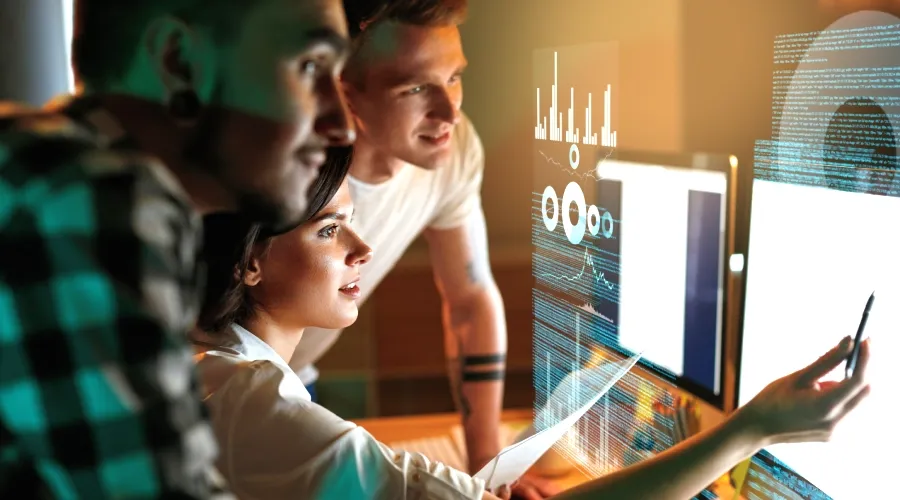 Team gathered around a computer with a 3D dashboard, representing AI driven total experience solutions.