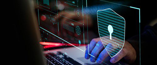 hands type on a laptop keyboard with a digital overlay showing a shield and padlock, indicating cybersecurity, set in a dimly lit environment with colorful electronic displays.