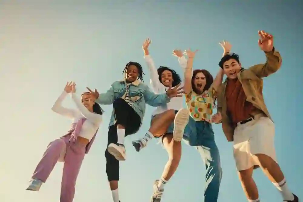 Friends jumping outdoors under a bright blue sky, symbolizing TP’s purpose driven by warmth, vibrancy, diversity, and passion.