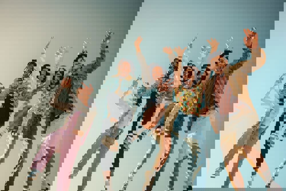 Friends jumping outdoors under a bright blue sky, symbolizing TP’s purpose driven by warmth, vibrancy, diversity, and passion.