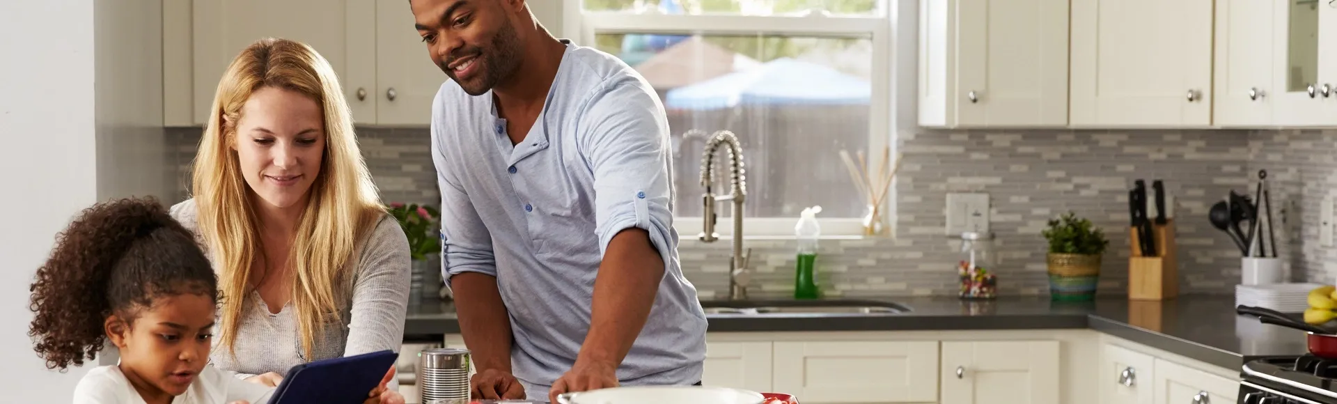 Family using a tablet together while preparing a meal in a modern kitchen.