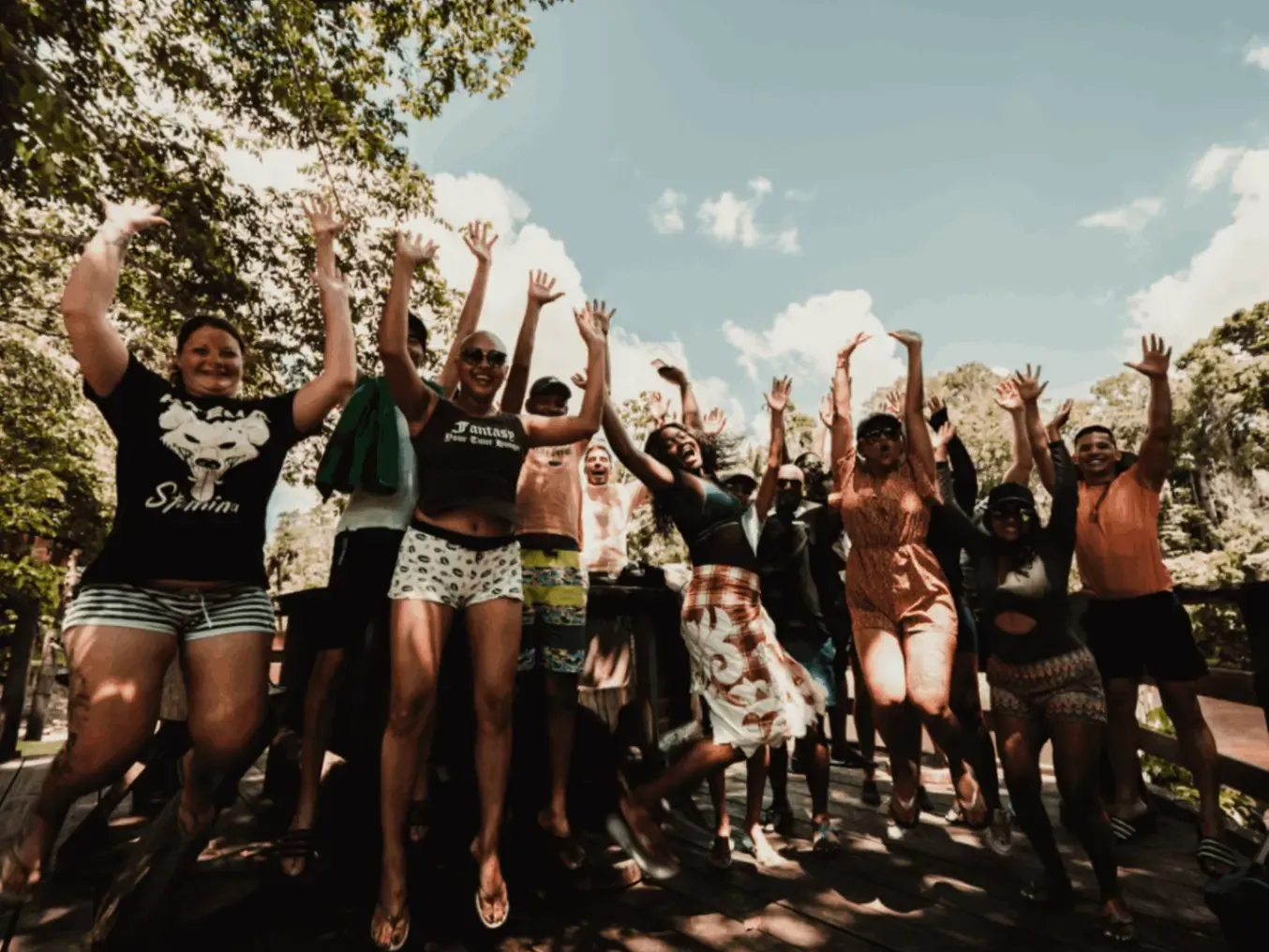Diverse people in front of trees with their hands up.