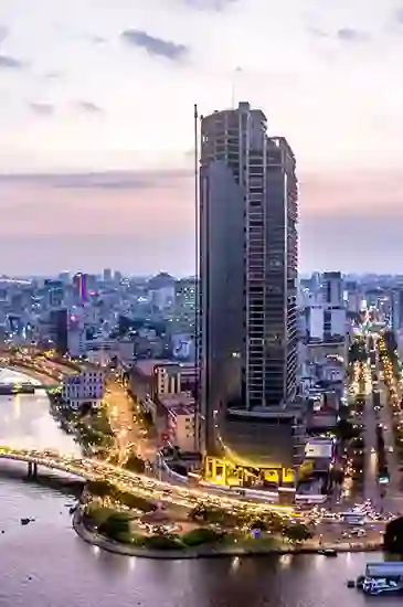 A tall skyscraper stands illuminated against a twilight sky, surrounded by urban cityscape and intersecting roads with bustling traffic.