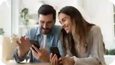 Smiling couple sit together at home and browsing smartphone