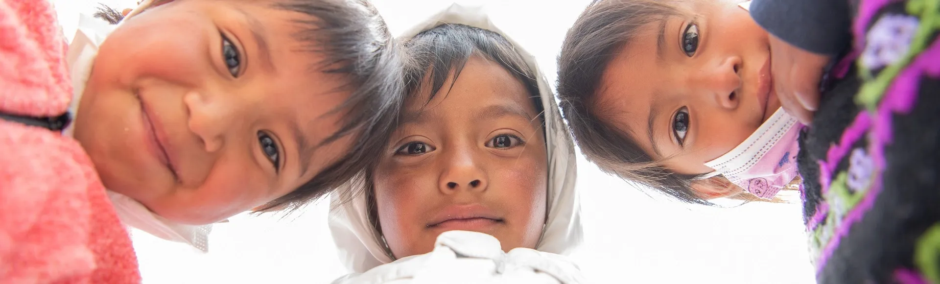 Three children looking down at the camera, smiling and curious.
