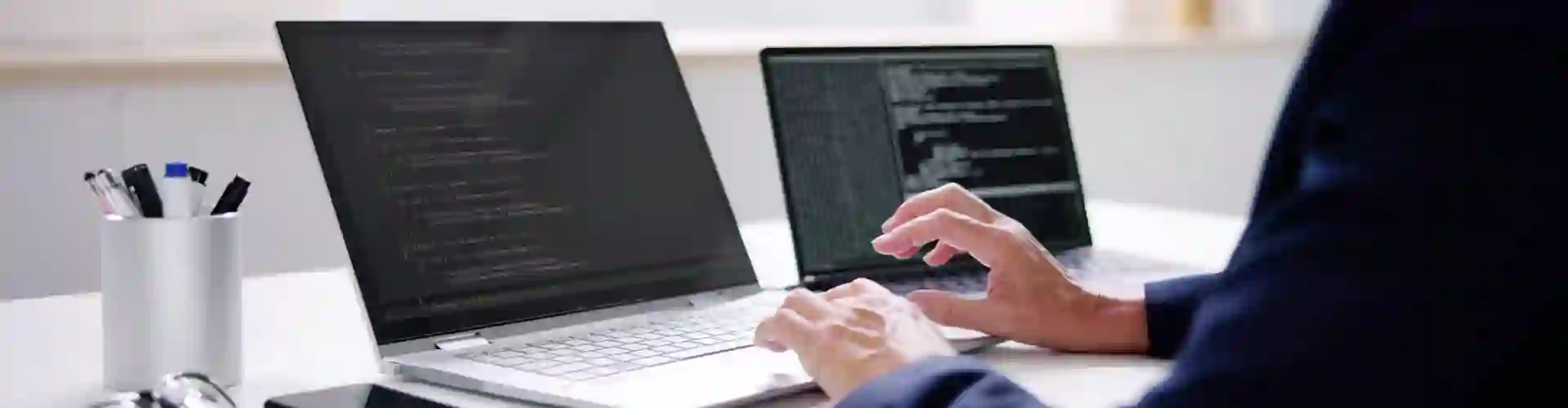 Person coding on two laptops, representing TP’s exploration of Agentic AI and its advanced technology applications