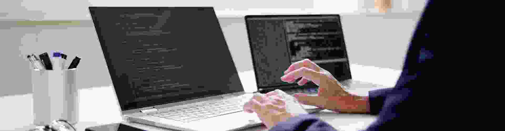 Person coding on two laptops, representing TP’s exploration of Agentic AI and its advanced technology applications