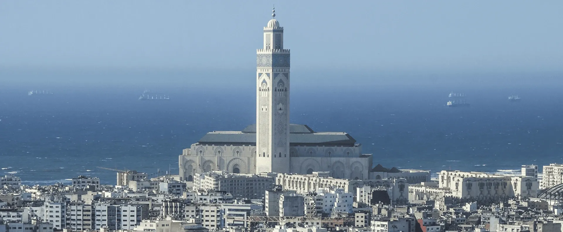 Aerial view of a Moroccan city with intricate architecture, narrow streets, and a beautiful blue ocean in the background.