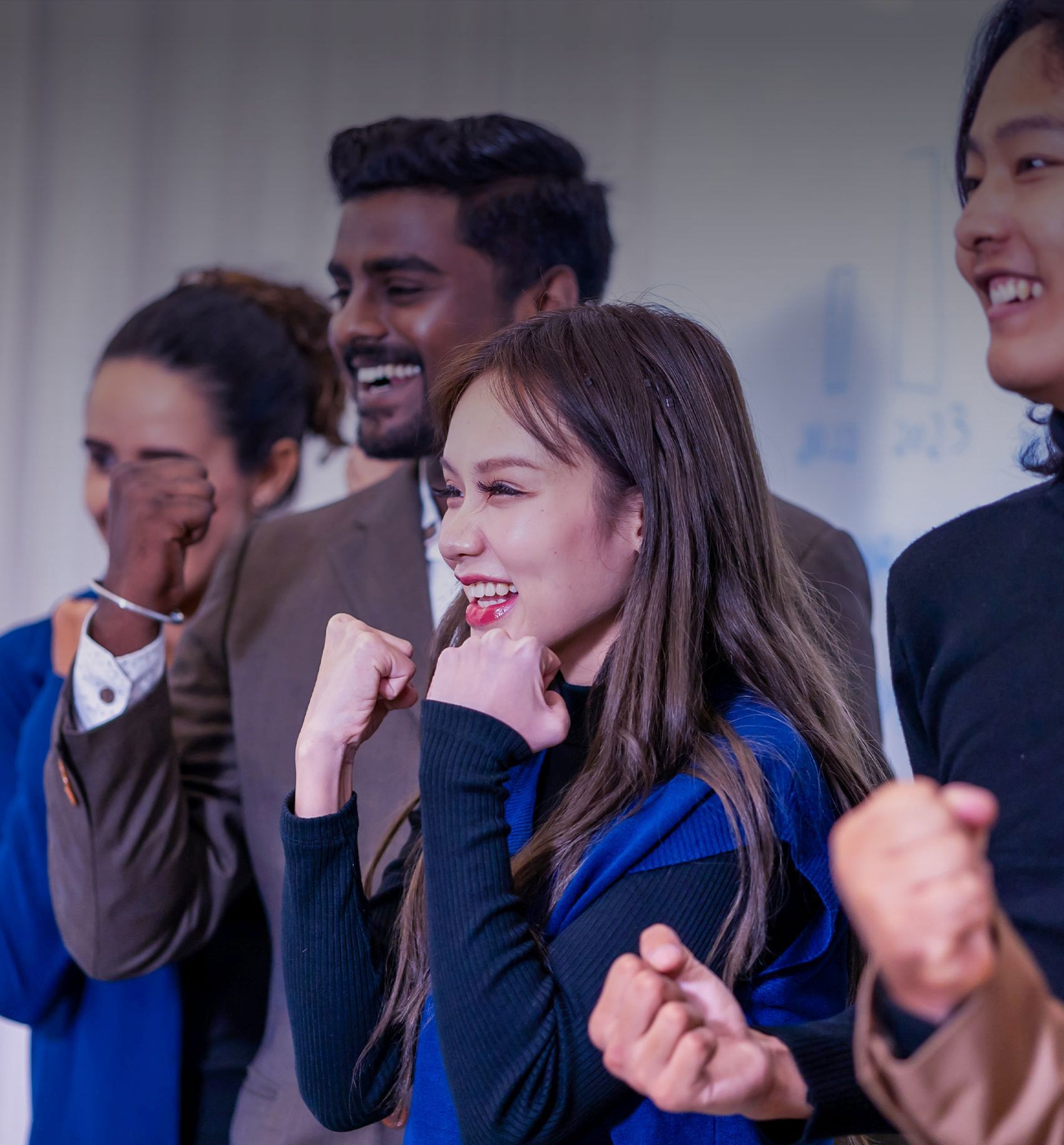 A diverse group of colleagues cheers enthusiastically, showing strong team spirit and excitement.