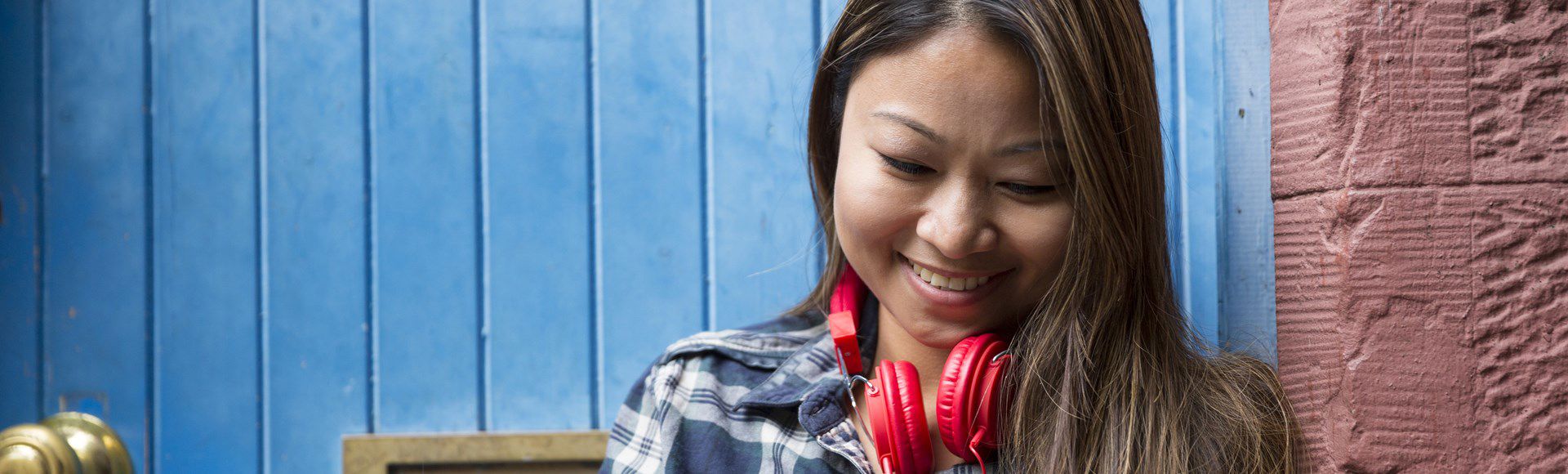 Smiling young woman with red headphones around her neck, symbolizing connection and positivity.