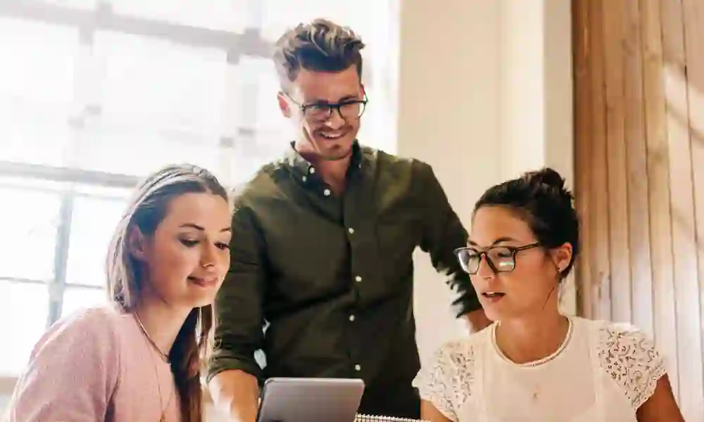 Three colleagues work together using a tablet, illustrating TP’s ai solution that accelerates onboarding in insurance services.