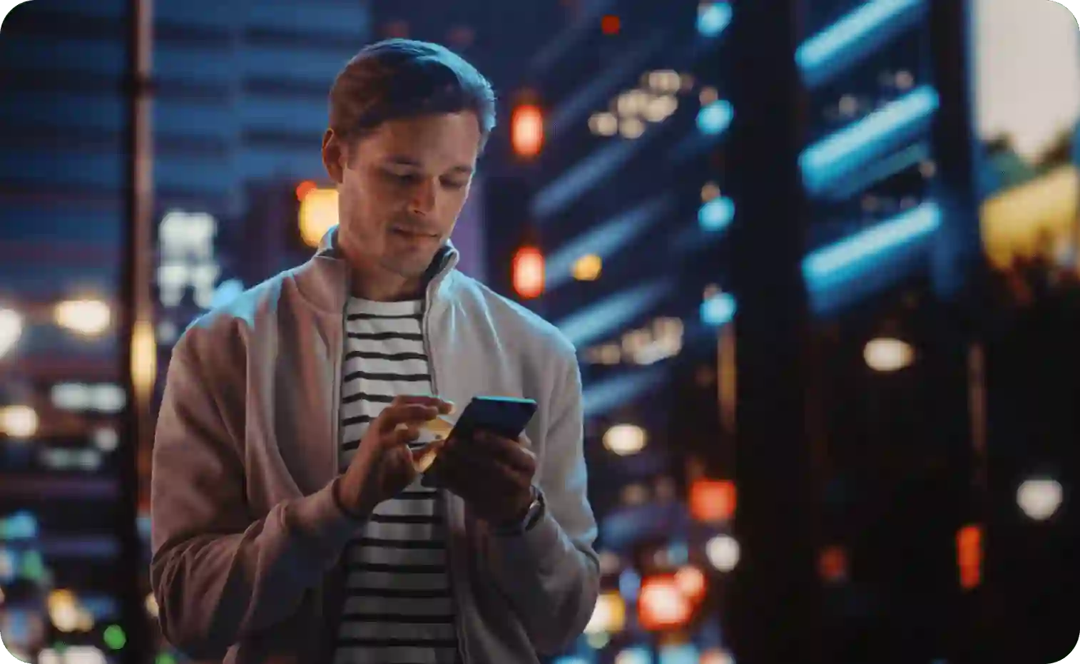 Man using smartphone on street under city lights at night
