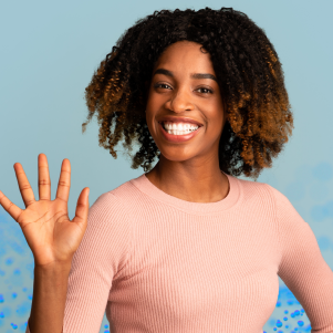 Uma pessoa sorri e acena com a mão direita, vestindo um suéter rosa. Ela está em frente a um fundo azul claro com pontos azuis espalhados abaixo.