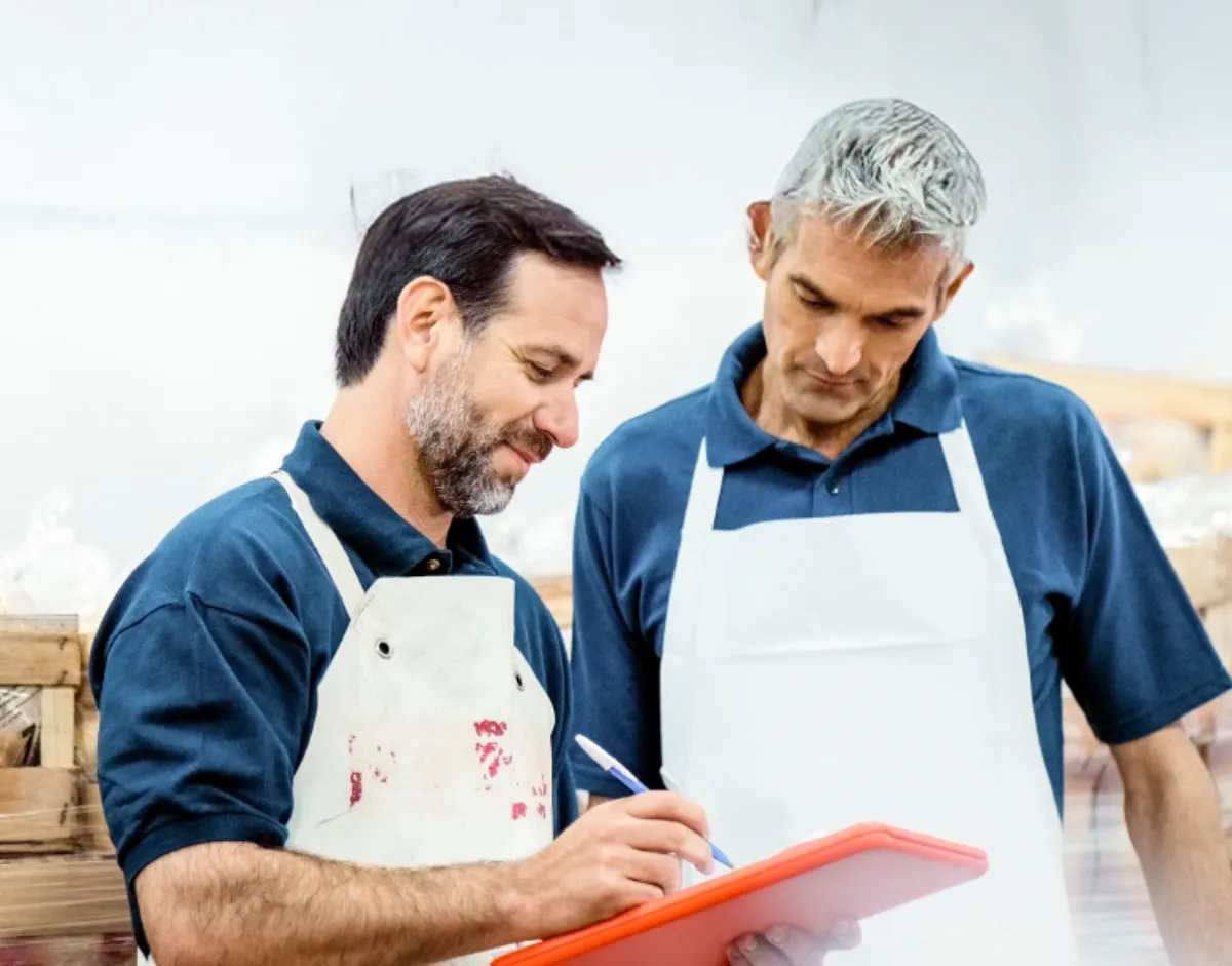 Two workers reviewing notes together in a production or warehouse environment.
