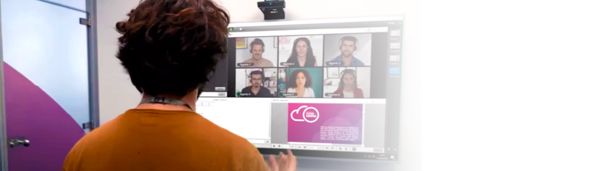 Pessoa participando de videoconferência com colegas exibidos em uma tela grande em escritório moderno